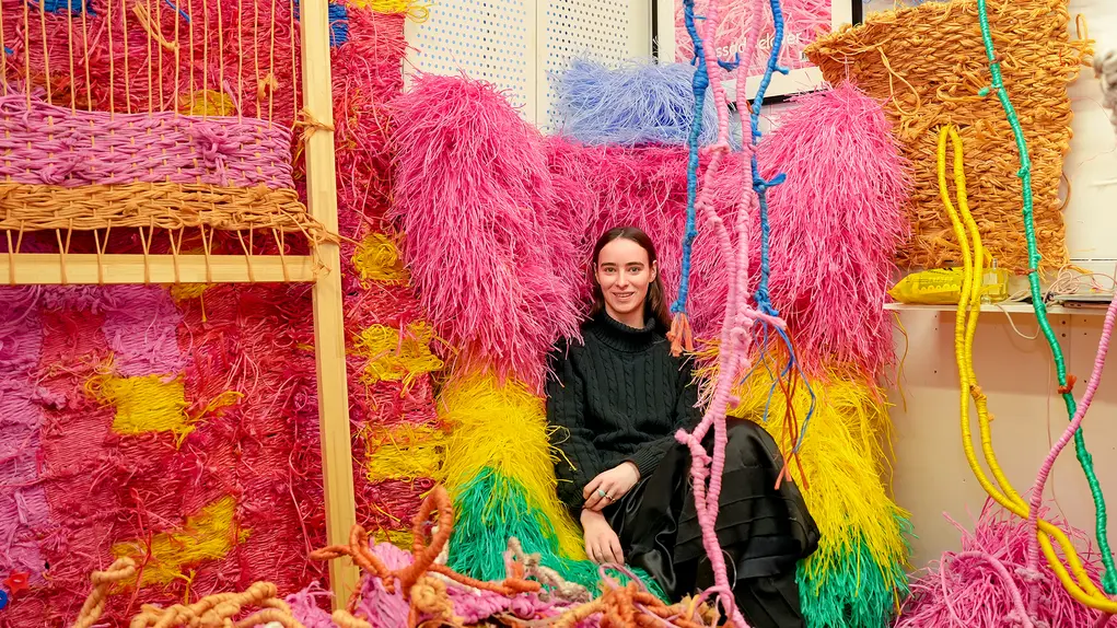 A woman in black sitting in a colourful studio of pink and yellow fabric artworks