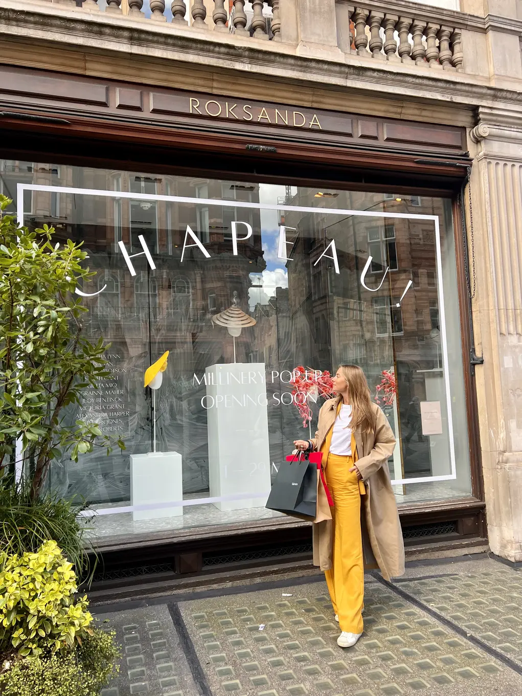 Yoannah Hanbury in a yellow trouser suit stands outside Chapeau! hat pop-up