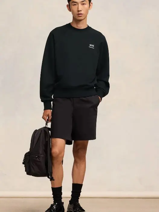 A man wearing black shorts, black sweatshirt and black backpack