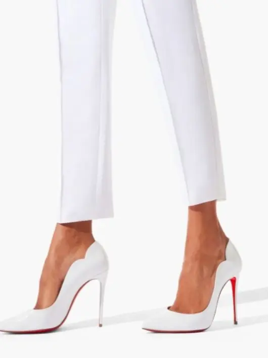 A woman's legs with white trousers and white stiletto heels