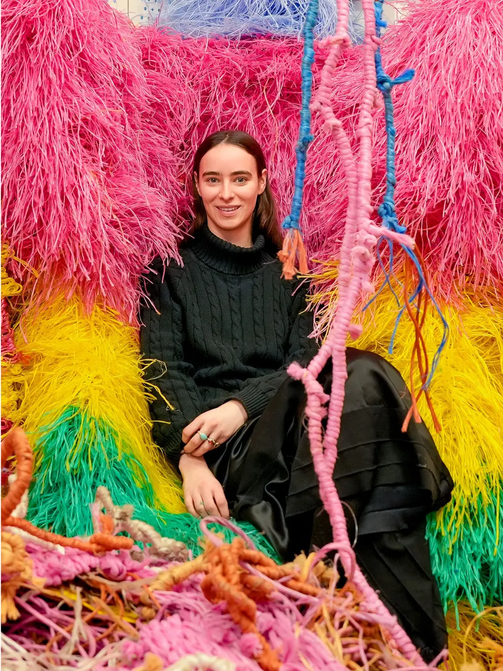 A woman in black sits on a colourful fabric artwork of pink, yellow and green