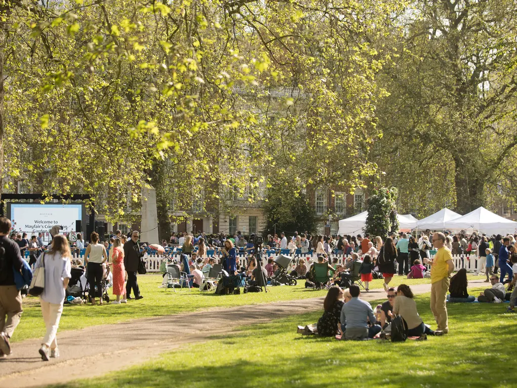 People sitting on the grass in Grosvenor Square face a big screen