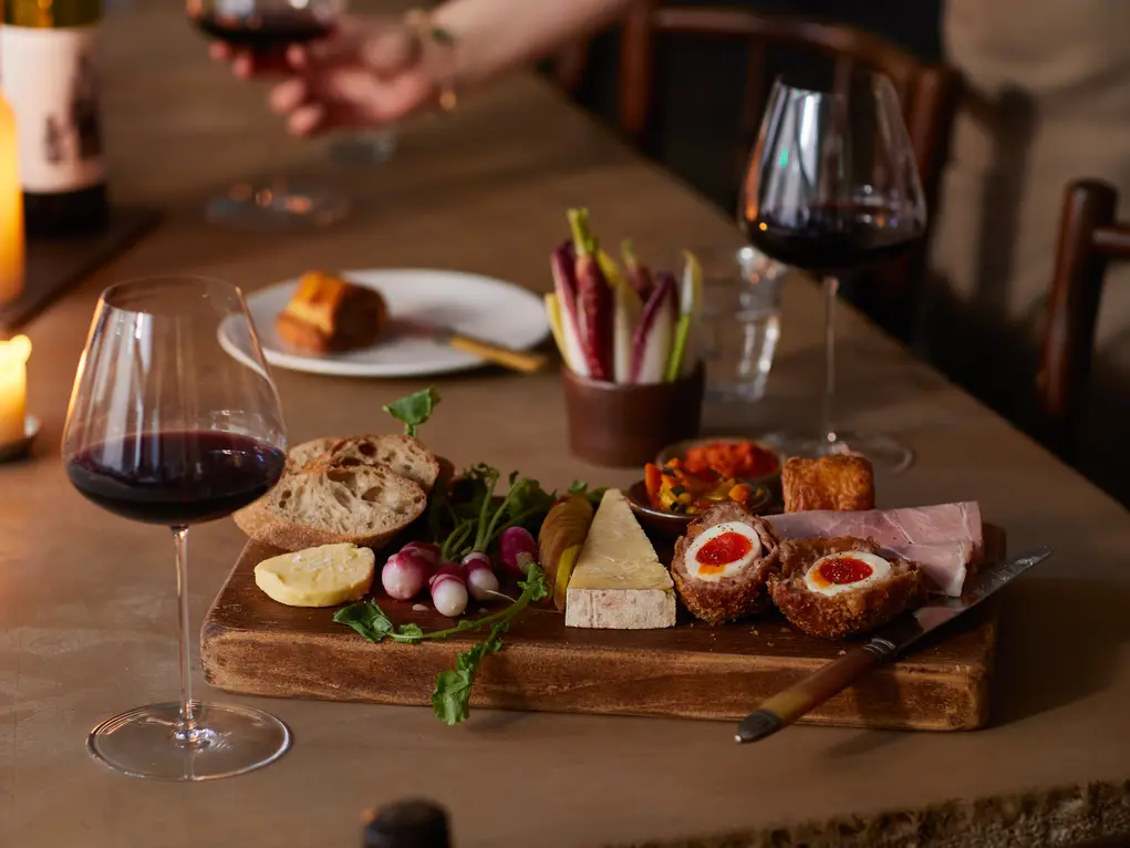 A wooden table with glasses of wine and cheese on a wooden board