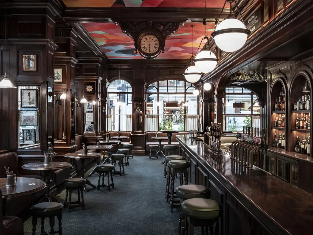 A long mahogany bar with circular tables and bar stools