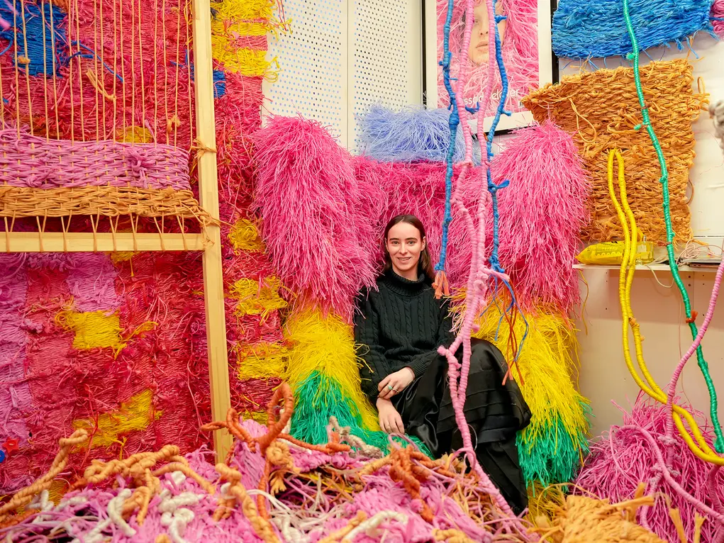 A woman in black sitting in a colourful studio of pink and yellow fabric artworks